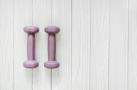 two lilac dumbbells lie on a white wooden background. horizontal banner, space for textの写真素材