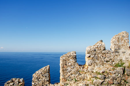 An old stone wall of an ancient fortress against the background of the sea and clear blue sky.の写真素材