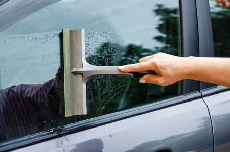 hand with squeegee brush washing car window. Manual car window cleaning with scraper.