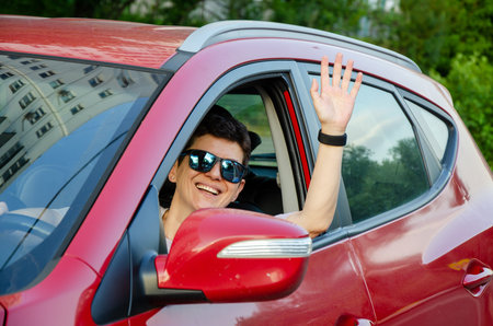 female driver waves hello while looking out of the window of her red carの写真素材