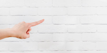 Female hand pointing with index finger at white brick wall, copy space, bannerの写真素材
