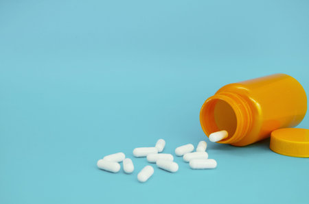 yellow bottle and scattered white capsules on blue background. Copy and text space