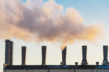 Industrial smoking chimneys against clear sunset sky. Concept of air pollution and environmental...