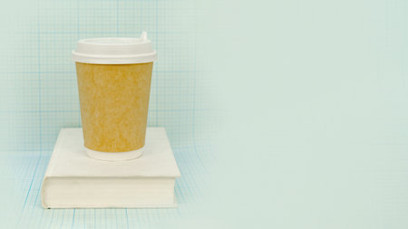 Coffee in a disposable paper cup and a white book on a light blue checkered background. Space for textの写真素材