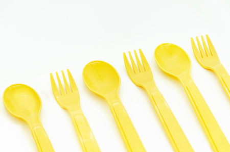Yellow plastic camping spoons and forks laid out in a row on a white background, copy space