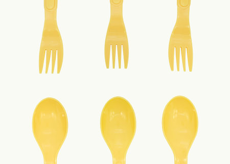 Yellow plastic camping spoons and forks laid out in a row on a white background, copy space