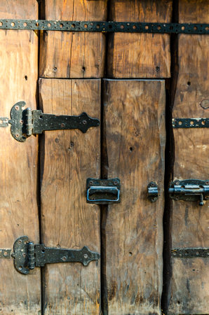 Rustic wooden door features aged metal hinges and latches, showing a weathered texture. The craftsmanship reflects historical design, creating a vintage, authentic appearance.の写真素材