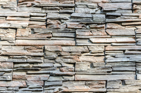 Close-up of a textured stone wall showing a rough surface pattern. Natural stones are arranged in layers, creating a rustic and weathered appearance suitable for backgrounds.の写真素材