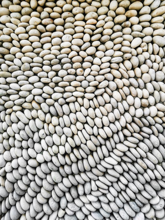 Collection of smooth, white pebbles arranged in an intricate, wavy pattern creating a visually appealing texture. Natural stones form a harmonious repetitive designの写真素材