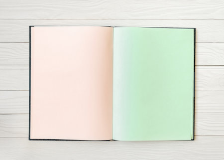 Open sketchbook displaying blank peach and mint-colored pages on a light wooden surface. This minimalistic design offers a perfect canvas for text or illustrations in a creative setting.の写真素材