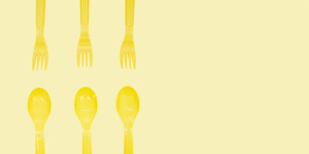 Yellow plastic forks and spoons are arranged in a grid pattern against a matching yellow background....