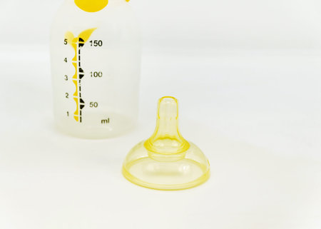 Close-up of a clear baby bottle with measurement markings and a yellow silicone nipple top placed on a white background. Essential infant feeding accessory.の写真素材