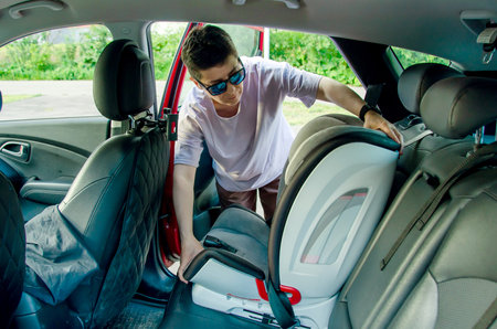 securing a child car seat in the back of a car, focusing on ensuring safety. The individual is positioned inside the vehicle, adjusting the seat for proper fitの写真素材