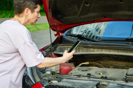 woman photographs a breakdown in the open hood of a carの写真素材