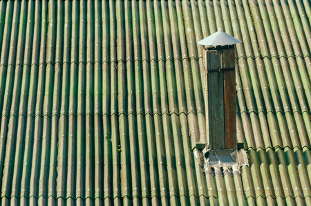 Aerial view of a corrugated green roof featuring a weathered wooden chimney pipe with a metal cap....