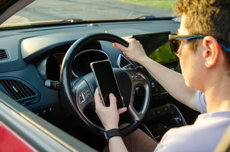woman Driver in a car focuses on a smartphone while controlling the steering wheel. This image...