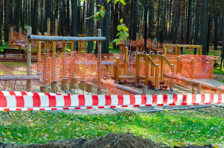 Playground in a forest area blocked off with orange safety netting and red-white tape for...