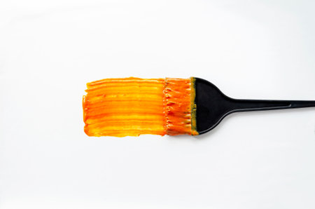 Hair dye brush strokes vivid orange color across a white background. The image highlights hair coloring tools and vibrant dye, emphasizing the transformation of hair color.の写真素材