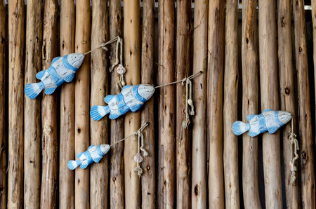 Wooden fish decorations are creatively hung on a rustic log wall, resembling a school of fish swimming. The arrangement adds a nautical and artistic touch to the wooden backgroundの写真素材