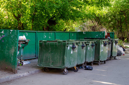 Dirty city dumpsters overflowing with garbage stand in a row