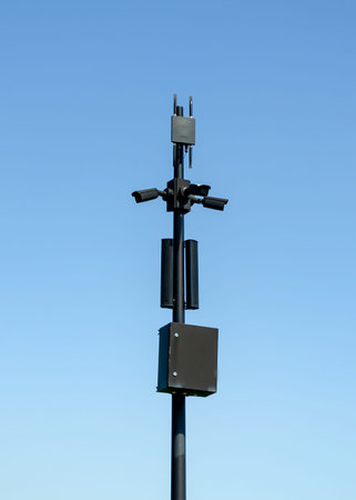 Surveillance cameras mounted on a tall pole with multiple devices attached, set against a clear blue...
