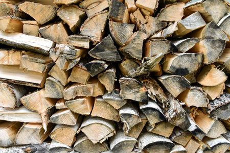 Closeup of stacked chopped firewood logs arranged in a rustic pile, showing wood texture, tree rings...