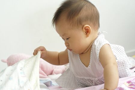 Cute infant finding something hidden under a blanket. Asian infant finding item under a blanket.の写真素材