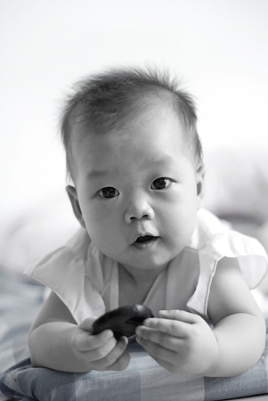 Cute Asian infant baby hold something and looking to her mother or farther.Black & White color image.の写真素材