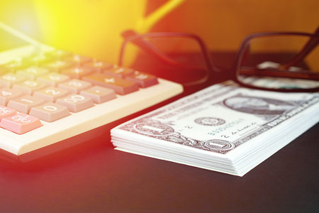 Piles of US dollar banknotes and financial calculator on black floor. warm tone color effect.の写真素材