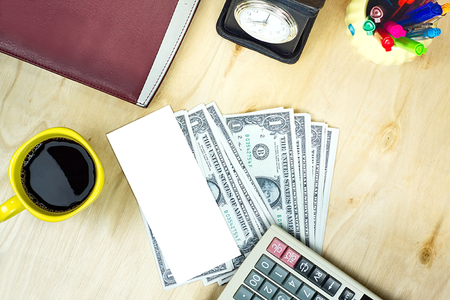 US dollar banknote and yellow cup of coffee with financial office supply on wood table background, for business financial conceptの写真素材