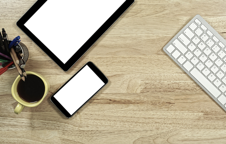 blank screen smartphones and tablet PC on the wooden desktop with computer keyboard and a cup of coffee in composition with copy space for your textの写真素材