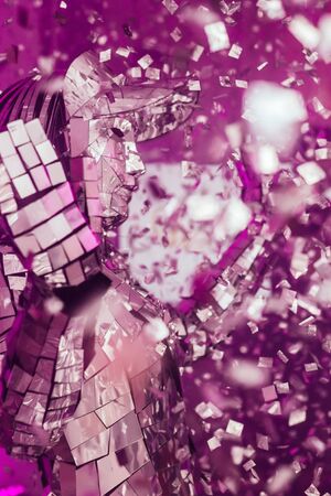 A guy at a party in a bright atmosphere with flying sweets in smoke in pink and blue lighting dancing with a disco ball on his headの写真素材