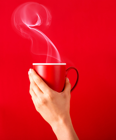 Woman with a cup of fragrant coffee in her hands on a cool day. Black warm coffee in cold weather.Coffee on a red background for your design. Advertising coffee.の写真素材