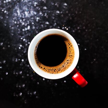 Fragrant black coffee in a cup. Smoke from black hot coffee. Advertising coffee. Glitter lights background. defocused.の写真素材