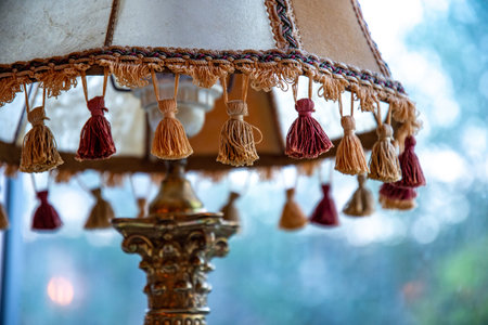 Closeup of brown tassels on antique lampshade with ornate bronze foot lamp element and blurry background. Vintage lamp details.の写真素材