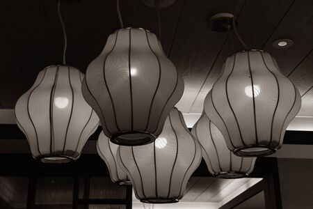 Retro lamps with geometric lampshades in shape of lanterns hanging under ceiling. Matte surface of traditional Chinese lamps with glowing light bulbs inside.の写真素材
