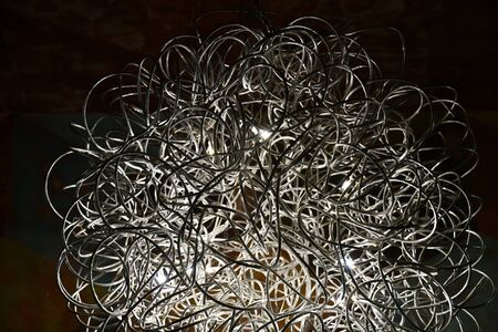 Curved entangled wires chandelier closeup. Silver tones metal wire lampshade. Contemporary interior lighting lamp. Abstract textured background. Curved lines chaotic pattern. Futuristic backdropの写真素材