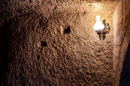 Ancient rough wall in cave with light from lamp in darkness. Antique lamp on scratched surface of limestone wall in cave of Cappadocia Turkey. Grunge backdrop.の写真素材