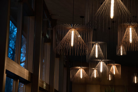 Wire chandeliers near windows. Contemporary metal lampshades. Lamps with long glowing light bulbs....