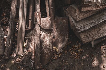 Old rusty metal shovels and dirty wooden planks stacked on ground in farmhouse yard. Grunge textures of old metal and wood materialsの写真素材