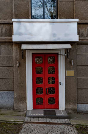 Kiev / Ukraine - 02 22 2020: Ornate red double door with rows of square shape windows and patterned metal gratings. Architecture in British style. Doorway of house facade with copy space on empty signboardのeditorial素材