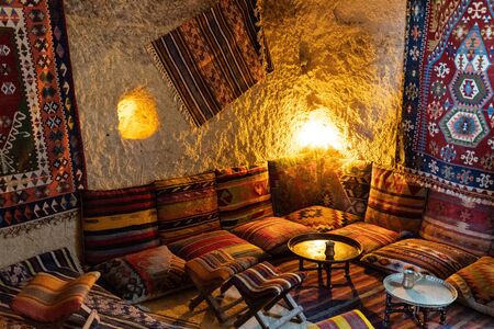 Traditional Turkish interior with vintage ornate carpets and cushions with striped ethnic ornaments. Small round coffee table in center of corner sitting zone in Asian interior. Turkish coffee time conceptの写真素材