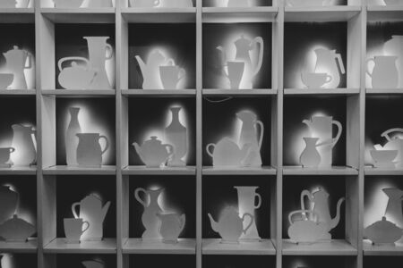Square shelves with various shapes of kitchen utensil and crockery. Teapot, cup, milk jug and sugar bowl silhouettes with backlight. Black and white photoの写真素材
