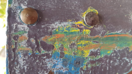 Old bolt heads and scratched paint on rough metal surface closeup. Metallic texture with strokes of yellow green blue colorsの写真素材