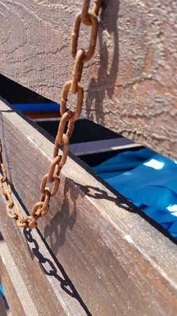 Rusty metal chains on rough weathered wood crate in bright sunlight. Vintage lock protection of old...