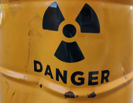 Black danger sign on yellow painted rusty metal barrel with rumpled damaged surfaceの写真素材