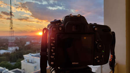 Odessa Ukraine - 08 27 2020: DSLR camera on tripod shoots sunset over city with cloudy sky and blurry silhouette of communication towerのeditorial素材