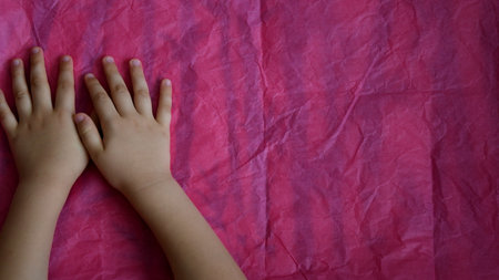 Toddler hands stop crumpled tissue paper on table. Directly above view of pink wrinkled paper and kid palms of hands touching paper textureの写真素材