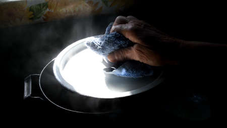 Granny hand open pan lid with rag. Hot water steam in bright light with dark shadowsの写真素材