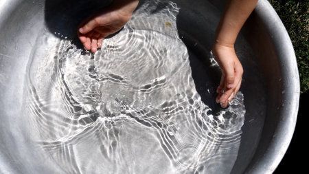 Little child trying to collect clear water in handful of hand palms. Toddler hands washing in old basin. Summer kids activity playing with transparent waterの写真素材